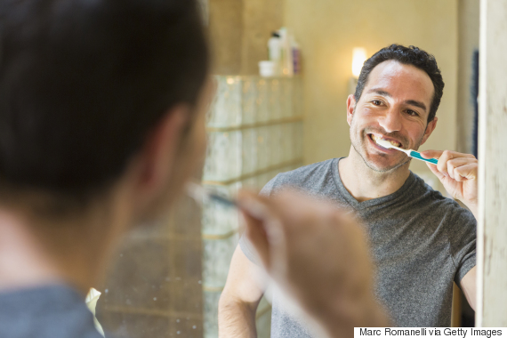 Hispanic man brushing teeth in mirror
